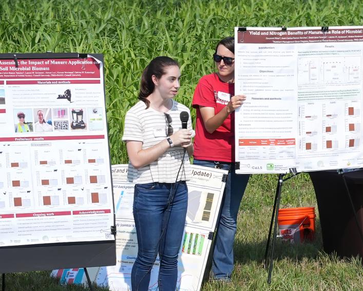 Sarah Flanagan speaking in front of a farm field and poster displays