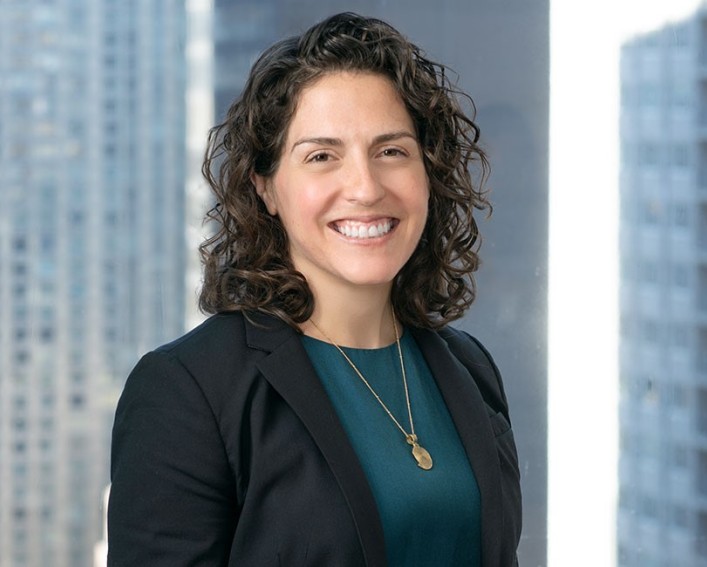 A headshot photo of Amanda Lefton, she has curly black hair and is wearing a teal shirt with a sport jacket.