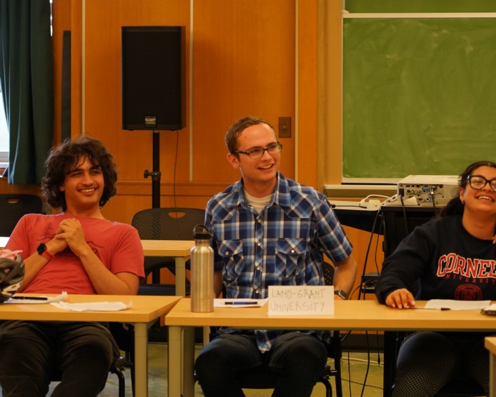 Three people smile at a table labeled with "land grant universities."