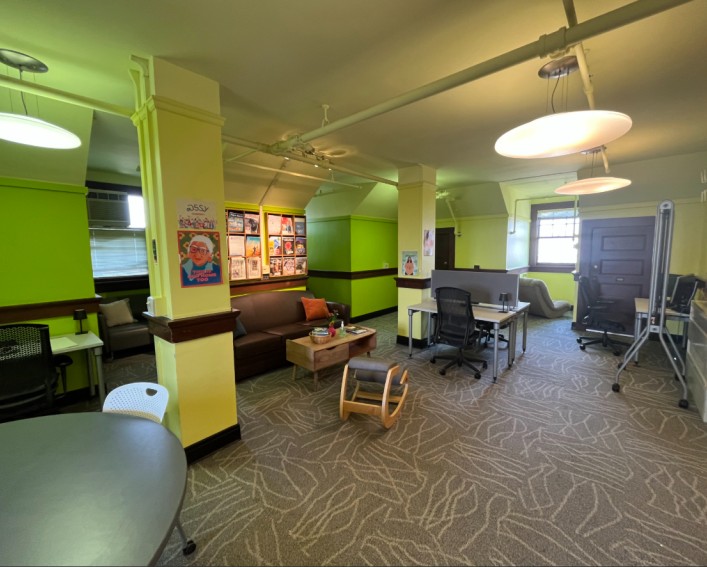 The student lounge, with green walls, a couch, desks, and chairs