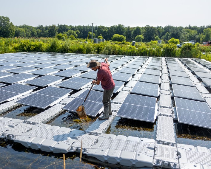 Person holding a net, stands on floating solar panels.