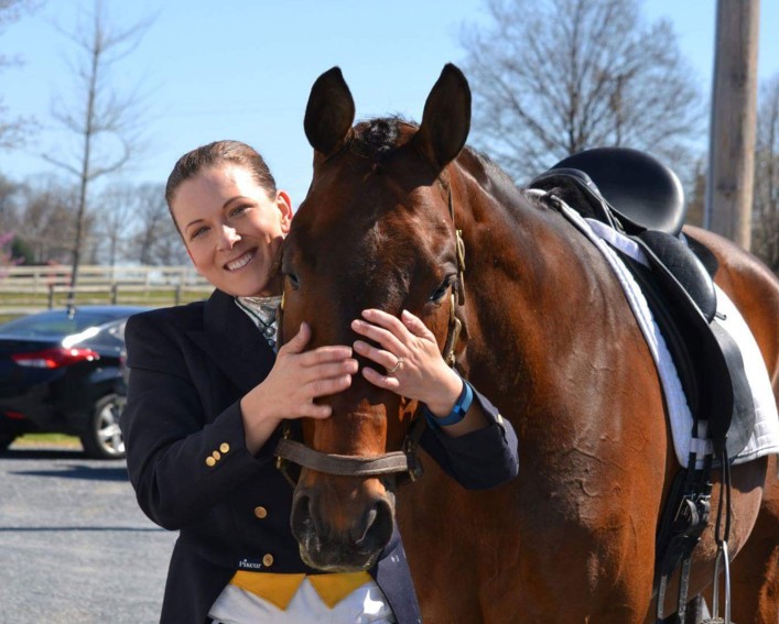 A headshot photo of Erika Machtinger smiling and standing with a brown horse