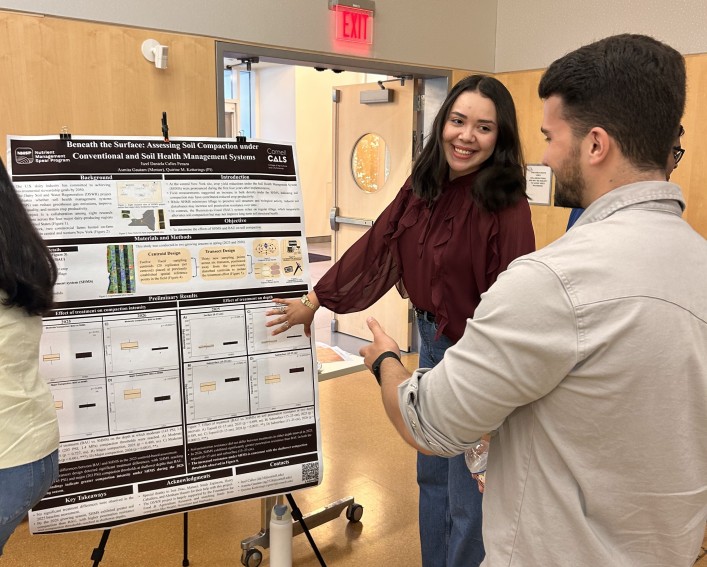 A woman gestures to her research poster while talking to a man.