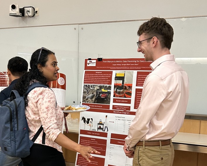 A woman (left) talks to a man (right) about research in front of his research poster.
