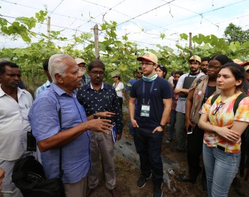 A man speaks to students standing in a field of crops