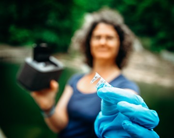 Faculty member holds water samples with a gloved hand.