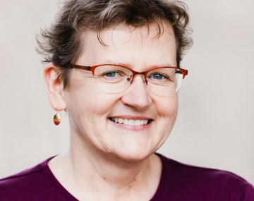 a woman with glasses and a maroon sweater in front of a gray background