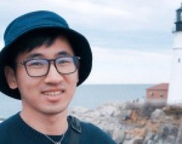 A man in a hat and glasses in front of a large body of water