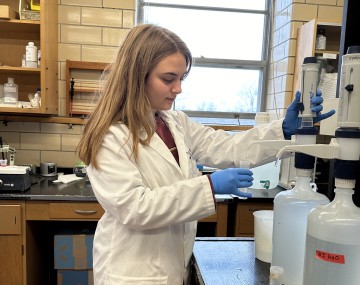 Woman in a lab coat pushing down the pump on a bottle.
