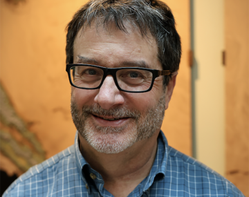 portrait of a man with glasses and a beard in front of a wood wall