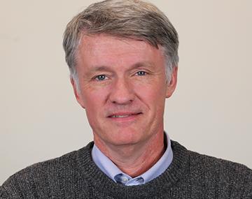 portrait of a man in a gray sweater in front of an off-white wall