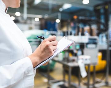 Person wearing a labcoat and a clipboard inside a food processing facility