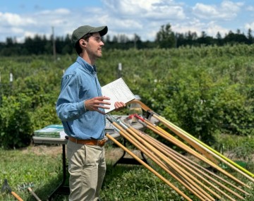 Bryan Brown giving a talk outdoors with weeding tools in the background