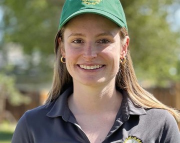 headshot of a smiling person with long light hair wearing a green cap