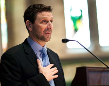 photo of a man in a suit at a podium with his hand on his chest