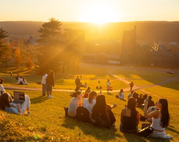 students sit watching the sunset on a sloped hillside