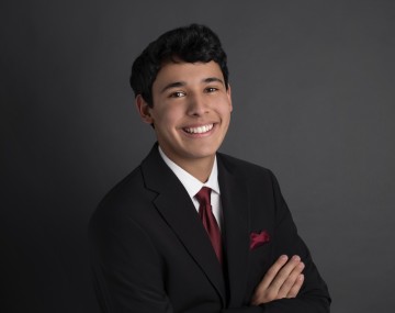 Adiitsai wears a black suit and smiles for the camera.