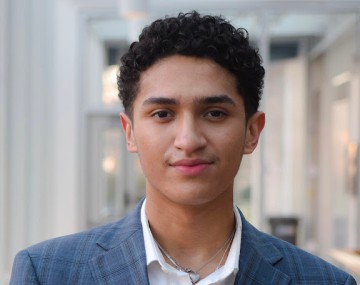 Student wearing a blue suite with a heart-shaped necklace