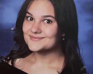 Student in a black dress, smiling in a graduation photo