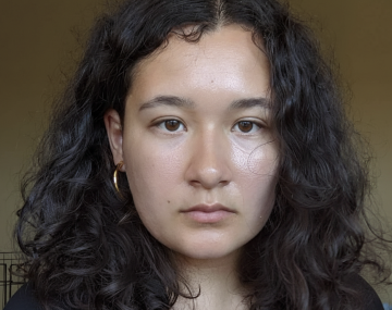 person with long curly dark hair in a black shirt with sleeves