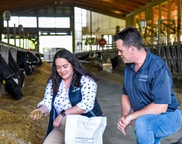 a man and a woman look at cattle feed in a barn