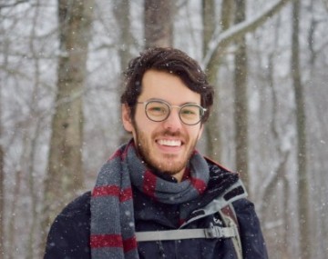 Photograph of a man with dark hair and glasses posing outside in the winter.