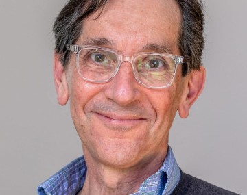 Professional portrait of a person wearing glasses, a blue shirt and grey sweater.