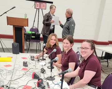 three girls sit behind a table with microphones in front of them
