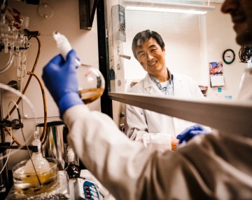 Researcher looks on as student holds up lab equipment