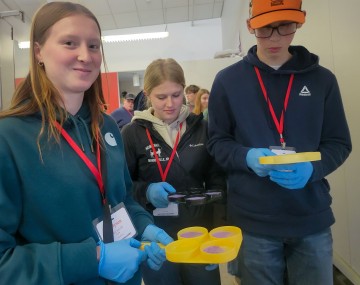 two girls and a boy stand holding containers with liquid in them