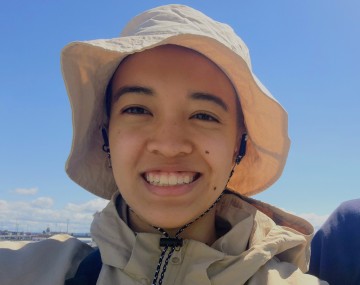 headshot of a person with a white hat and beige jacket with blue sky