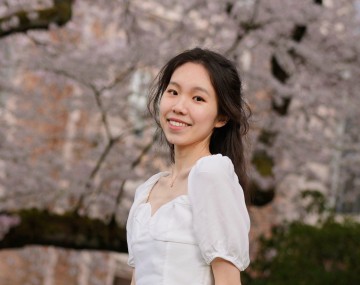 person with long dark hair and white top under blossoming tree