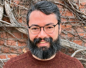 a man with a beard and a brown sweater in front of a wall